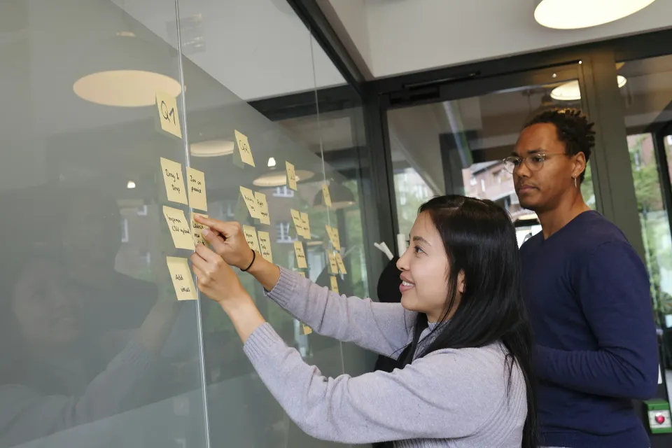 Two people in a workshop placing sticky notes on a glass wall during a collaborative planning session.